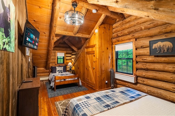 Spacious upstairs bedroom with queen and twin beds, TV, and warm log cabin vibes—great for families or groups.