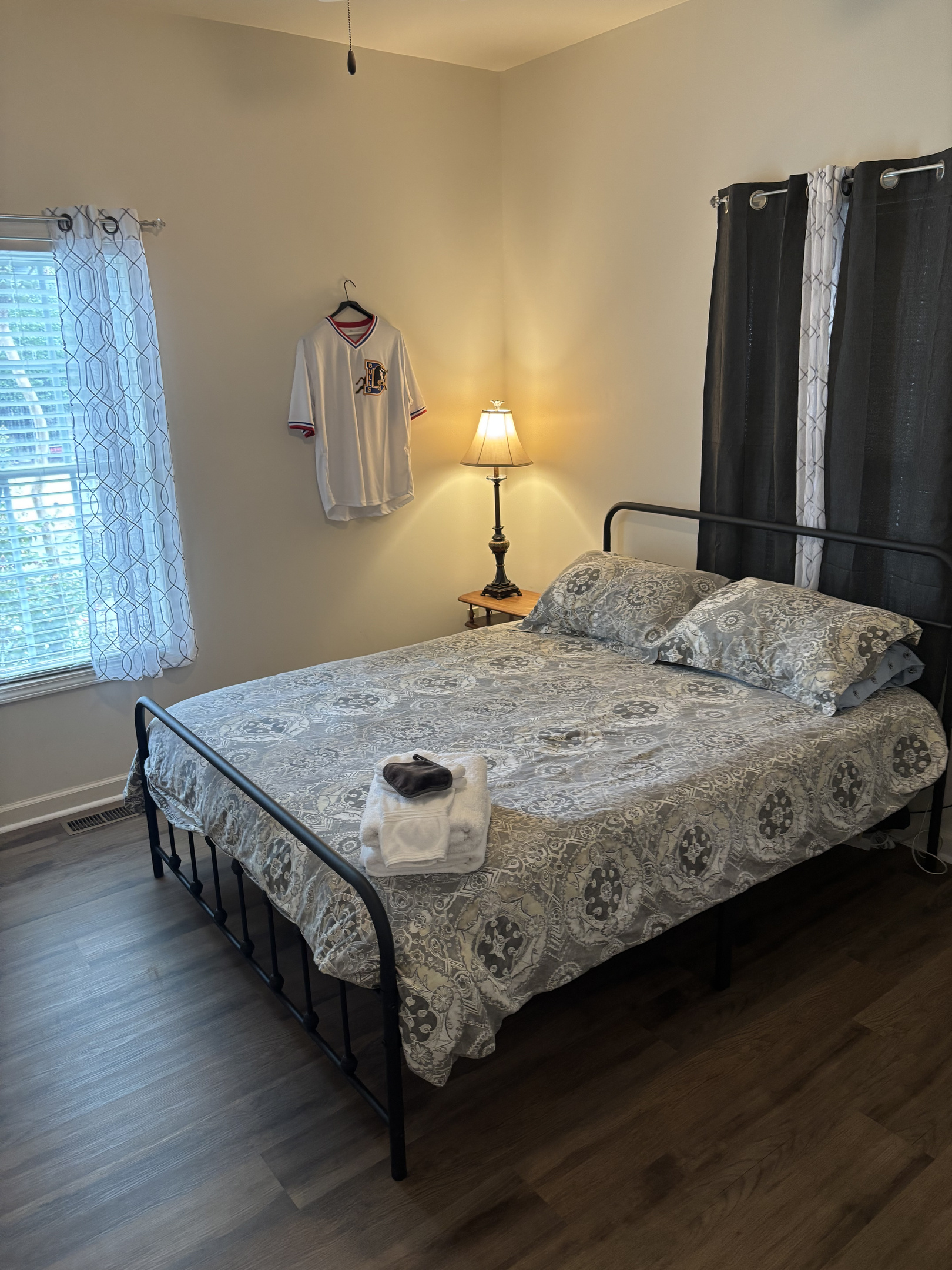 Bright queen bedroom with blackout curtains, bedside lighting and fresh guest-ready linens.