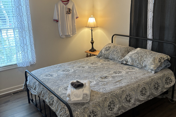 Bright queen bedroom with blackout curtains, bedside lighting and fresh guest-ready linens.