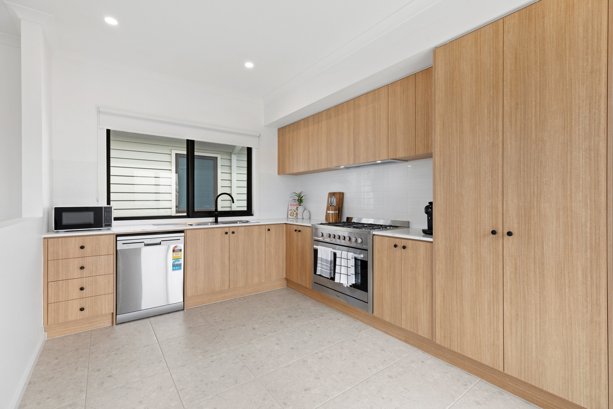 Kitchen with timber cabinetry, stainless-steel oven with gas cooktop, dishwasher and a microwave on the bench, plus a window over the benchtop.