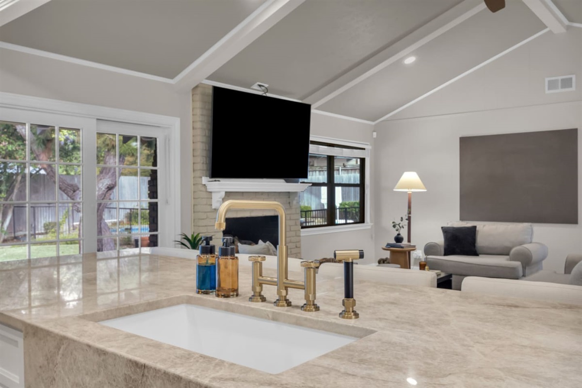 Open-concept living and kitchen area featuring a 70” Smart TV, fireplace, spacious seating, luxe kitchen with granite countertops, five-burner gas stove, double oven, island seating, and a fully stocked coffee bar.