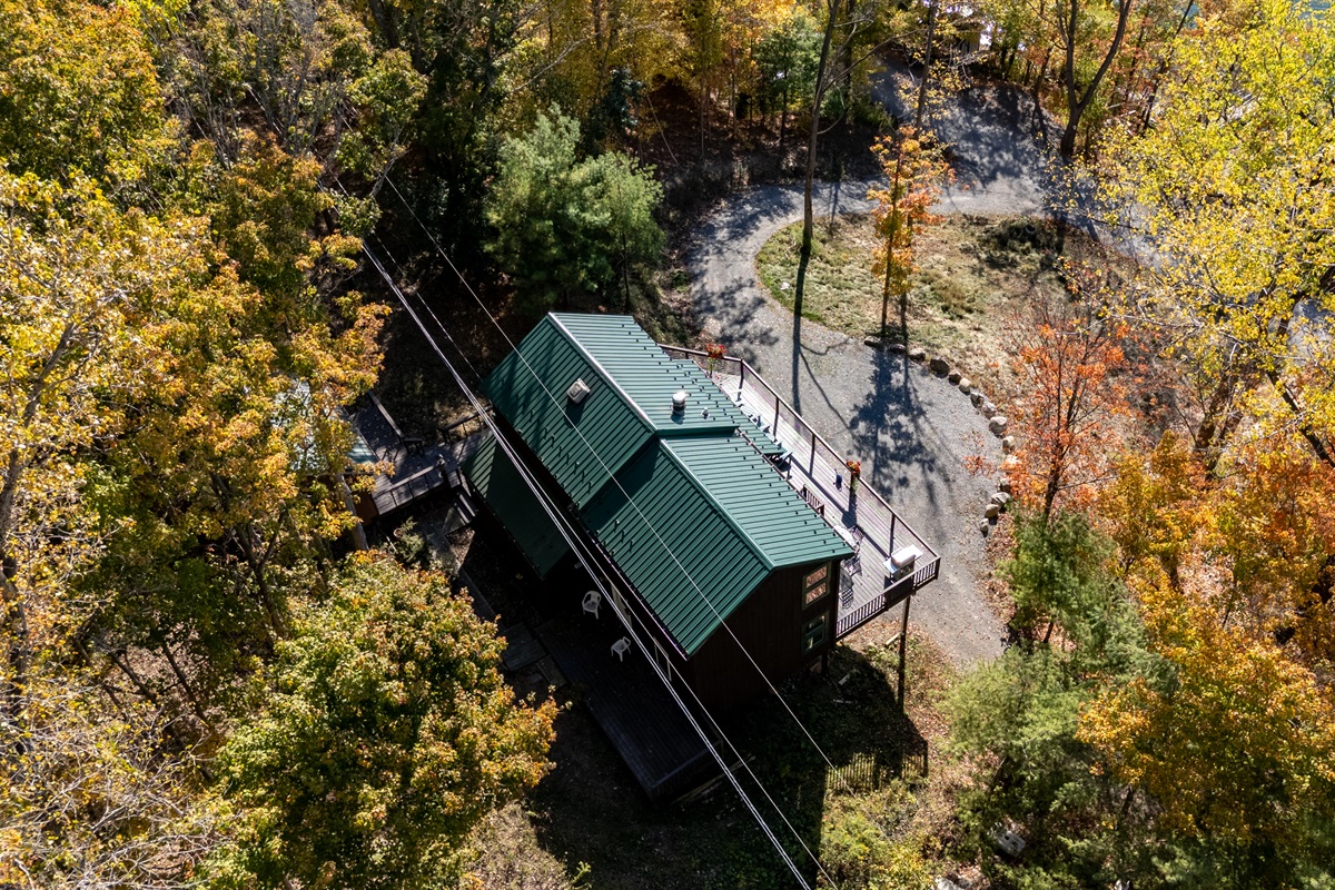 Side aerial view of the cabin with wrap deck and fall foliage backdrop.