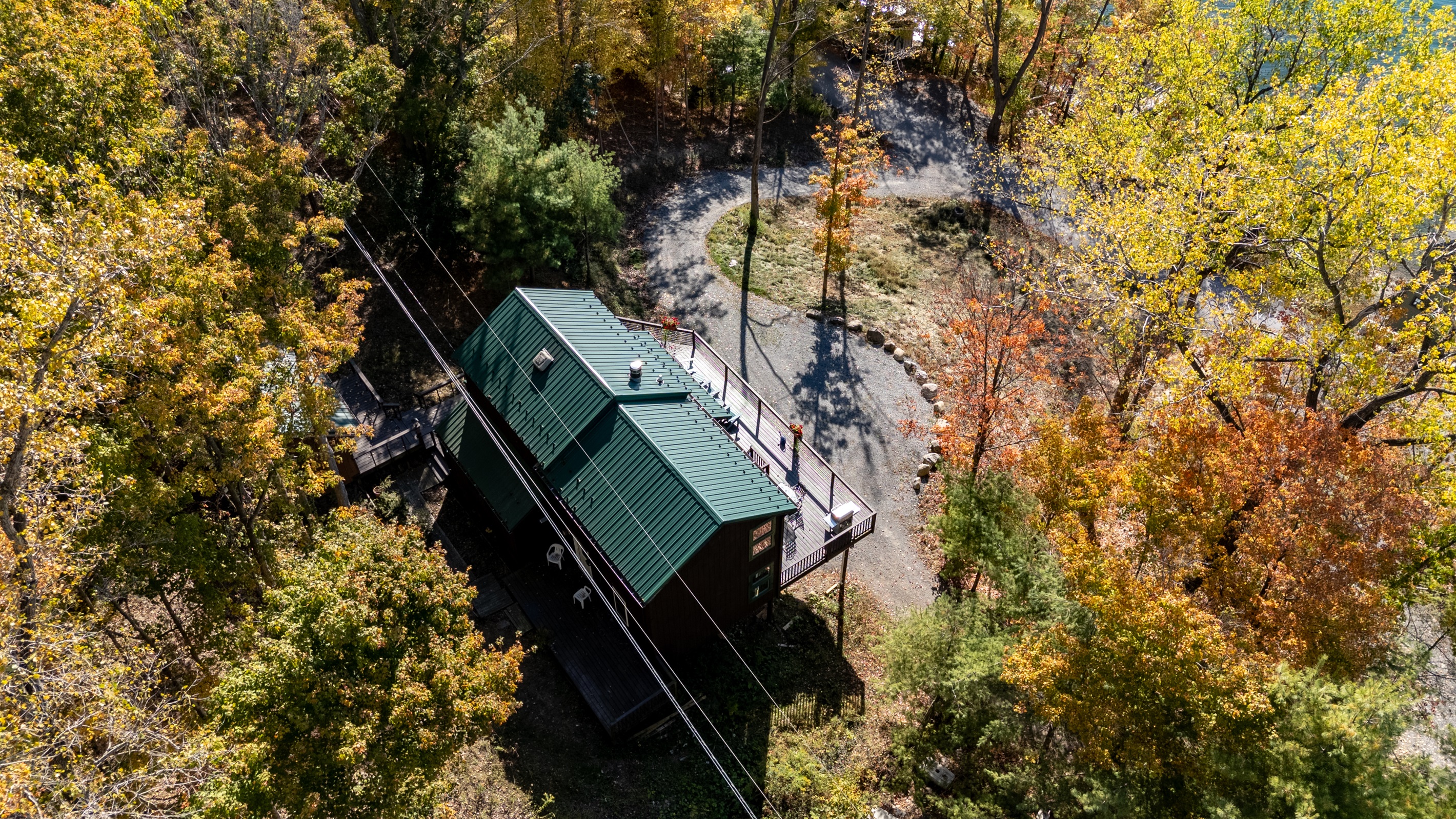 Side aerial view of the cabin with wrap deck and fall foliage backdrop.
