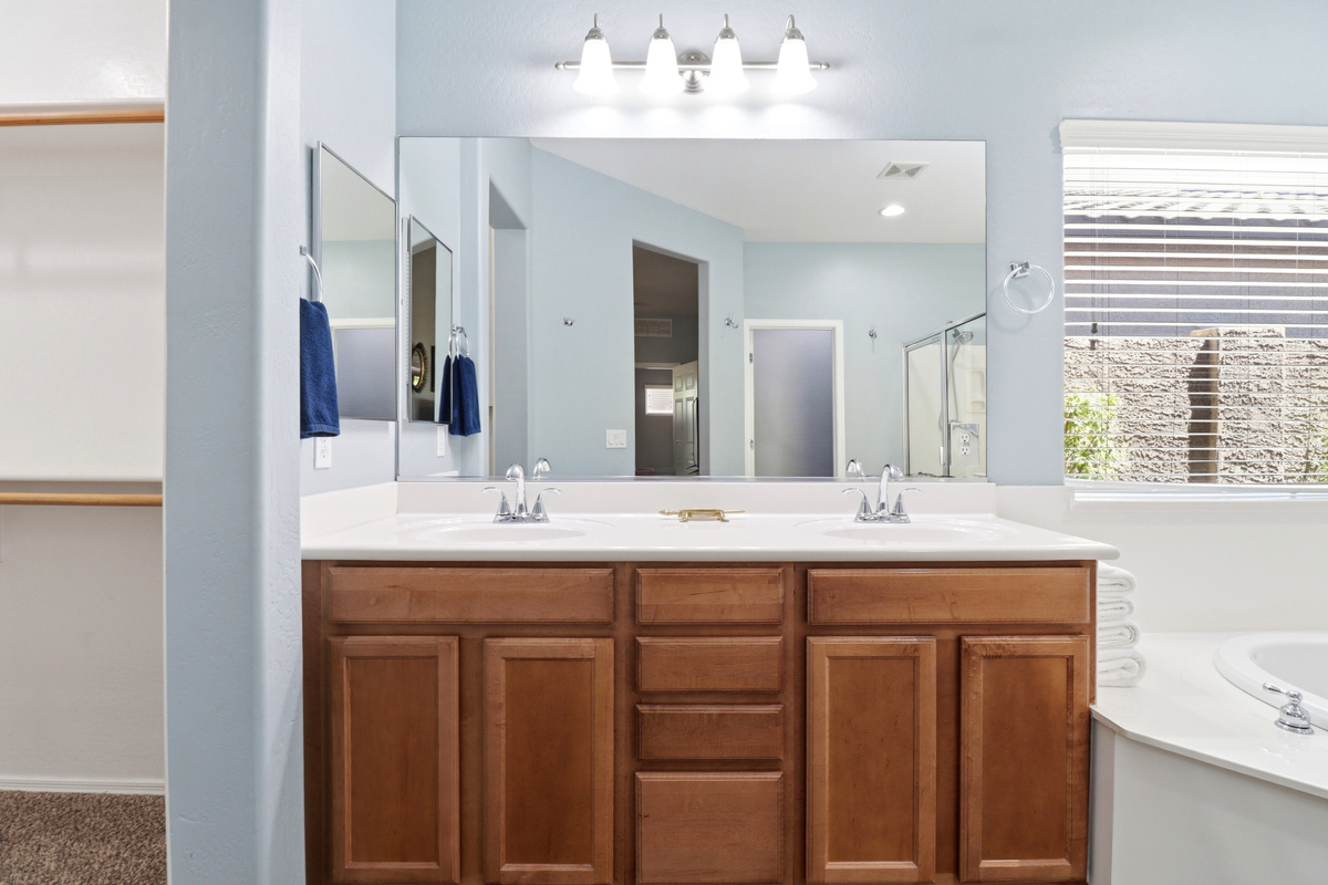 Full bathroom with double sinks, wood vanity storage, and a soaking tub nearby.
