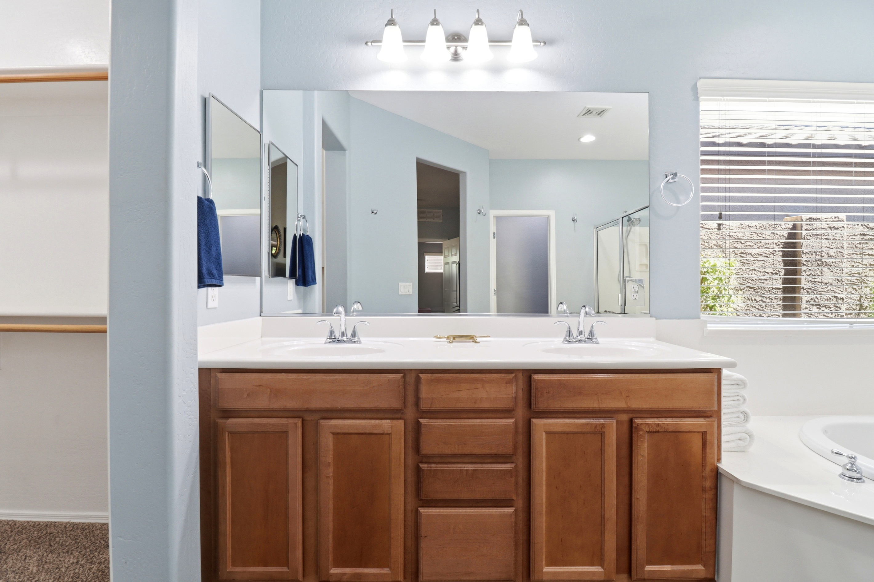Full bathroom with double sinks, wood vanity storage, and a soaking tub nearby.
