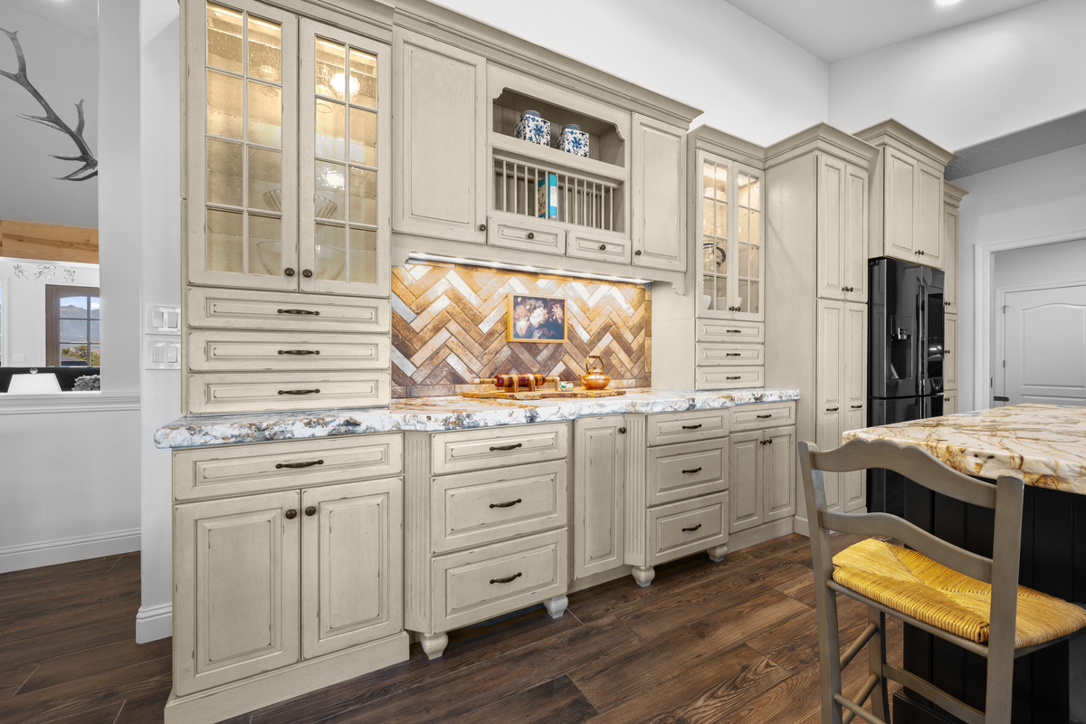 Detailed cabinetry, illuminated glass-front storage, elegant hardware, and a patterned backsplash give the kitchen a distinctive, upscale character.