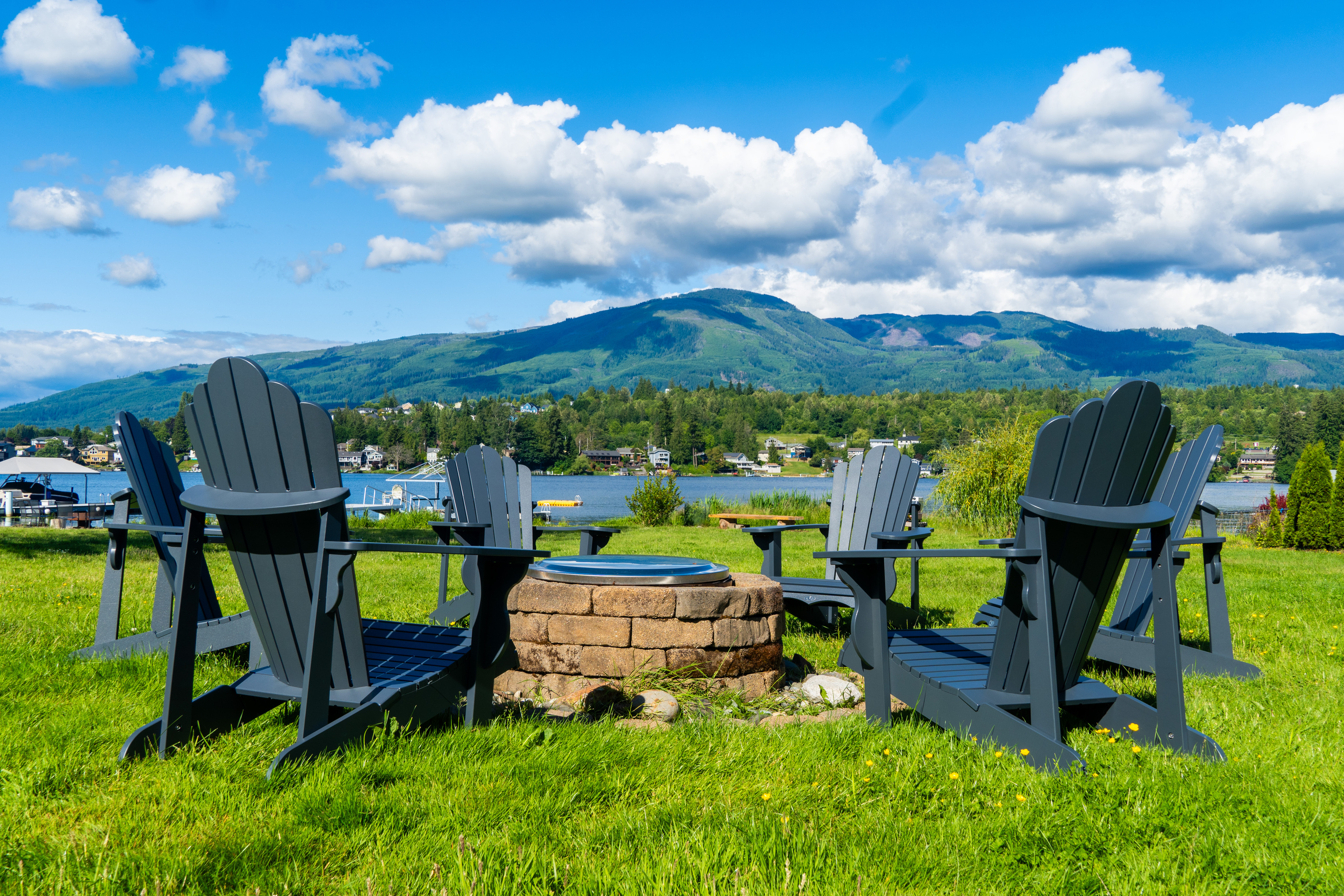 A wide, green backyard stretches to the lake, with a dock and fire pit ready for evenings outdoors. The open lawn feels inviting, and the calm water reflects the shoreline, creating a peaceful connection between land and lake.