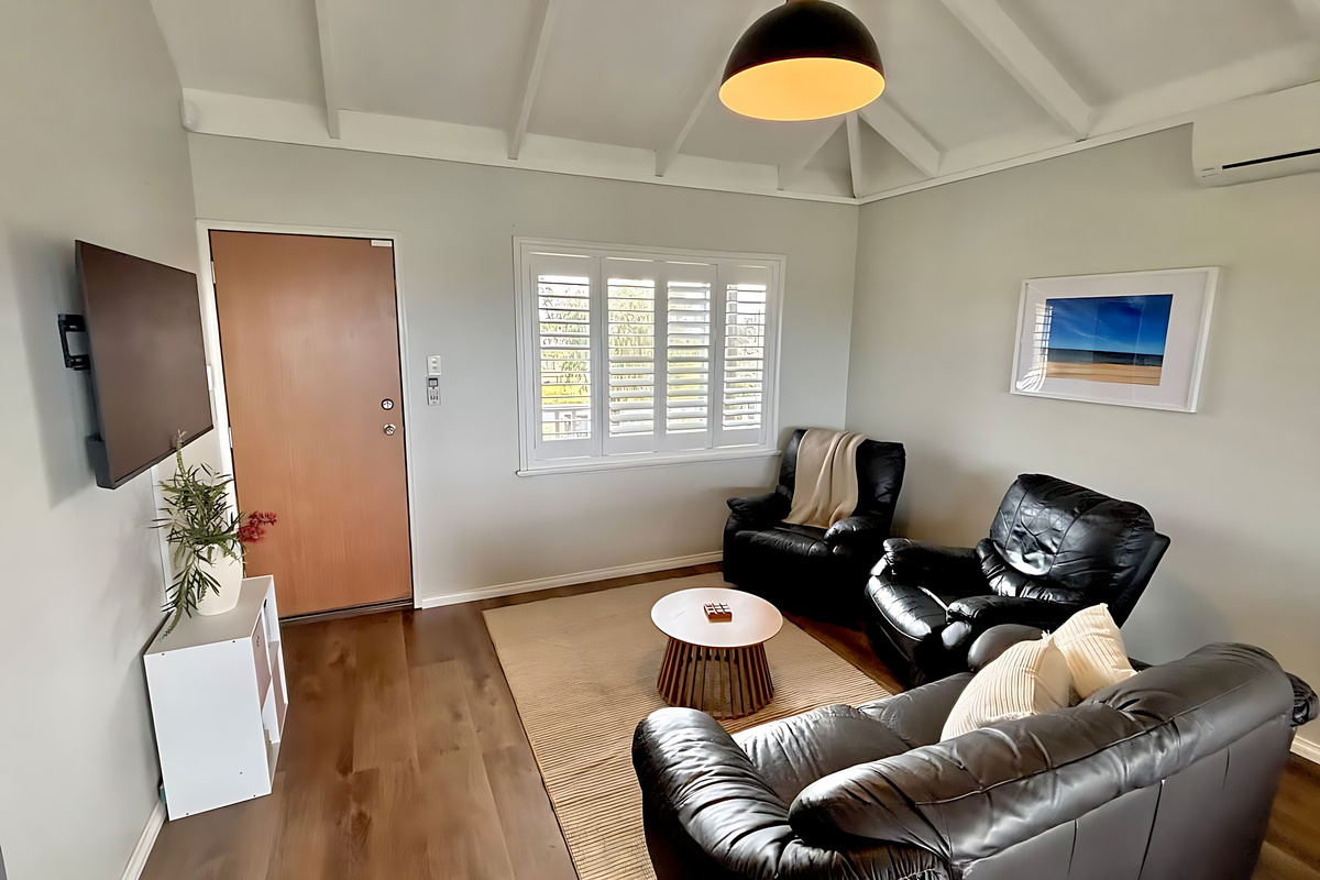 Two leather recliners and a lounge face the smart TV in the Preston Beach living room, with plantation shutters, a split-system air conditioner and a jute rug under the round coffee table.