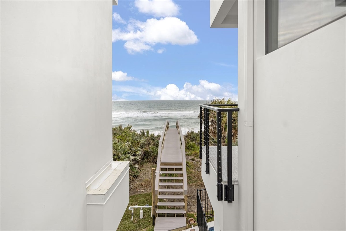 Admire the exterior of the house with a scenic bridge leading to the sea, complemented by a spacious balcony perfect for enjoying the view, all under a beautiful, cloudy sky that adds to the tranquil atmosphere
