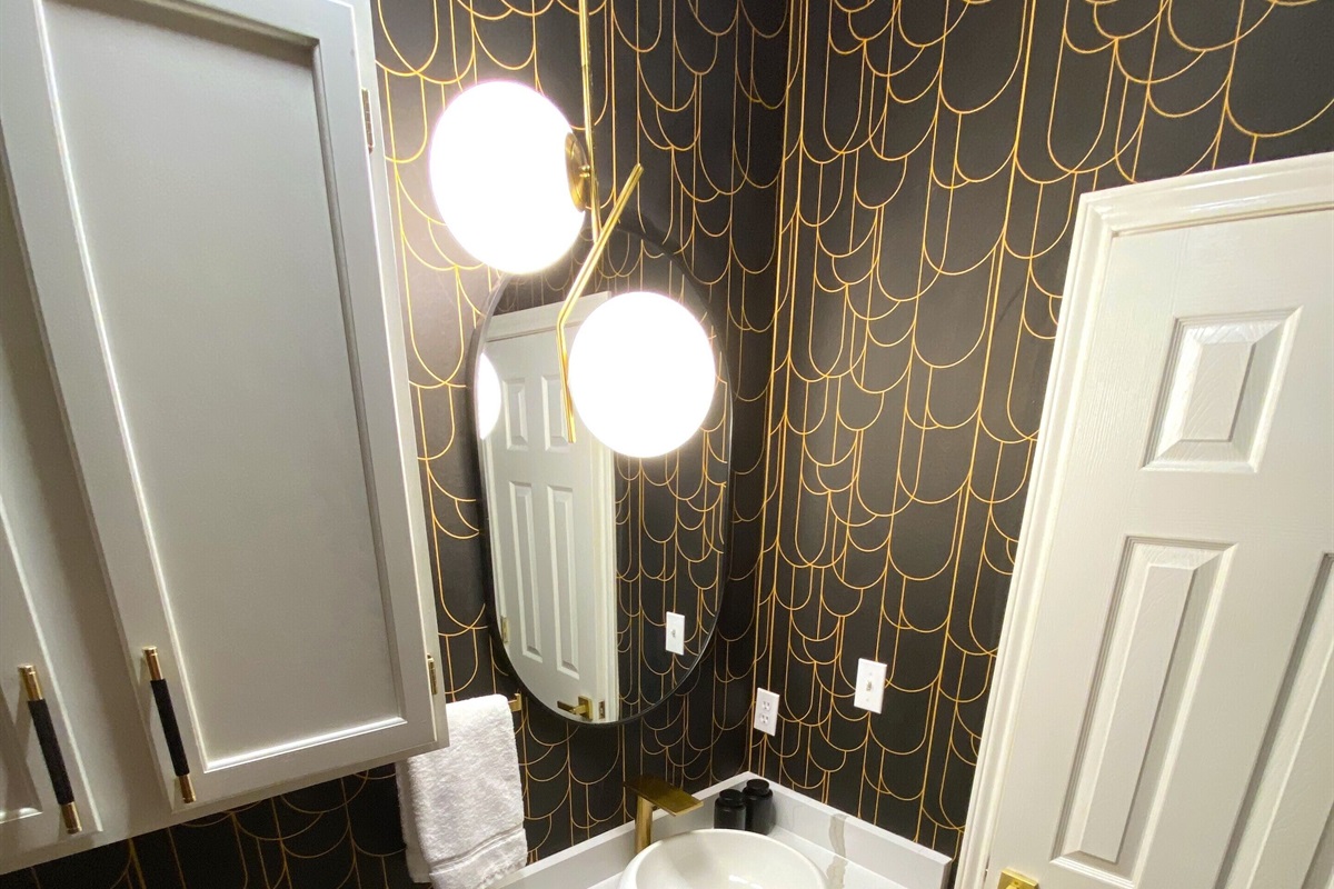 Welcome to this chic powder room, where bold black and gold wallpaper steals the show. The sleek vanity and modern lighting add a touch of luxury, making this the perfect spot for a quick refresh with a dash of style!