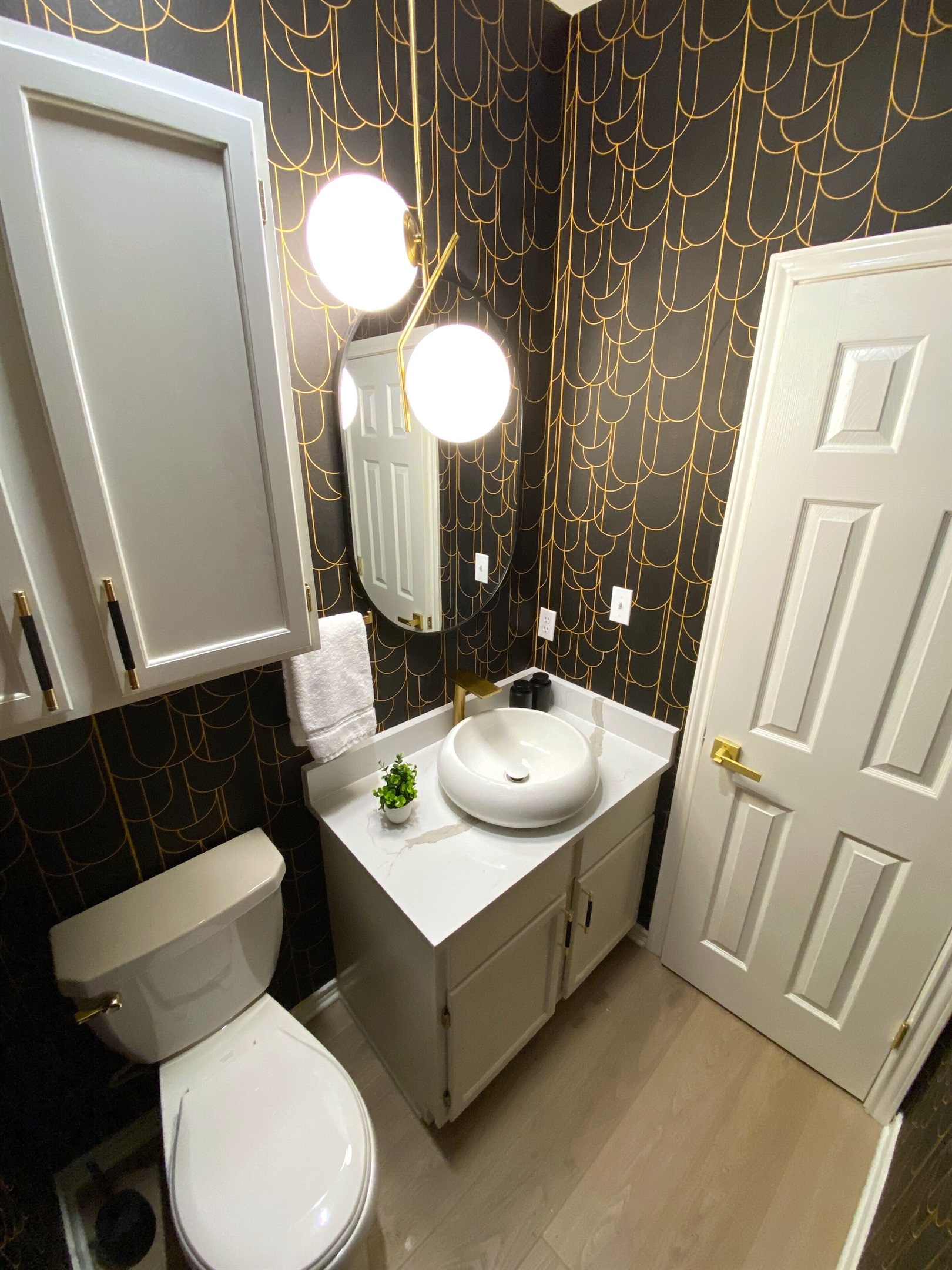 Welcome to this chic powder room, where bold black and gold wallpaper steals the show. The sleek vanity and modern lighting add a touch of luxury, making this the perfect spot for a quick refresh with a dash of style!