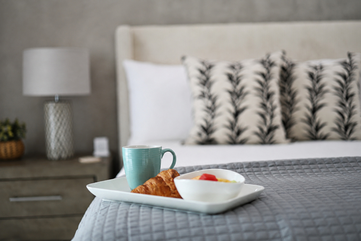 Enjoy a quiet morning with coffee, a croissant, and fresh fruit served on a soft, neatly made bed.