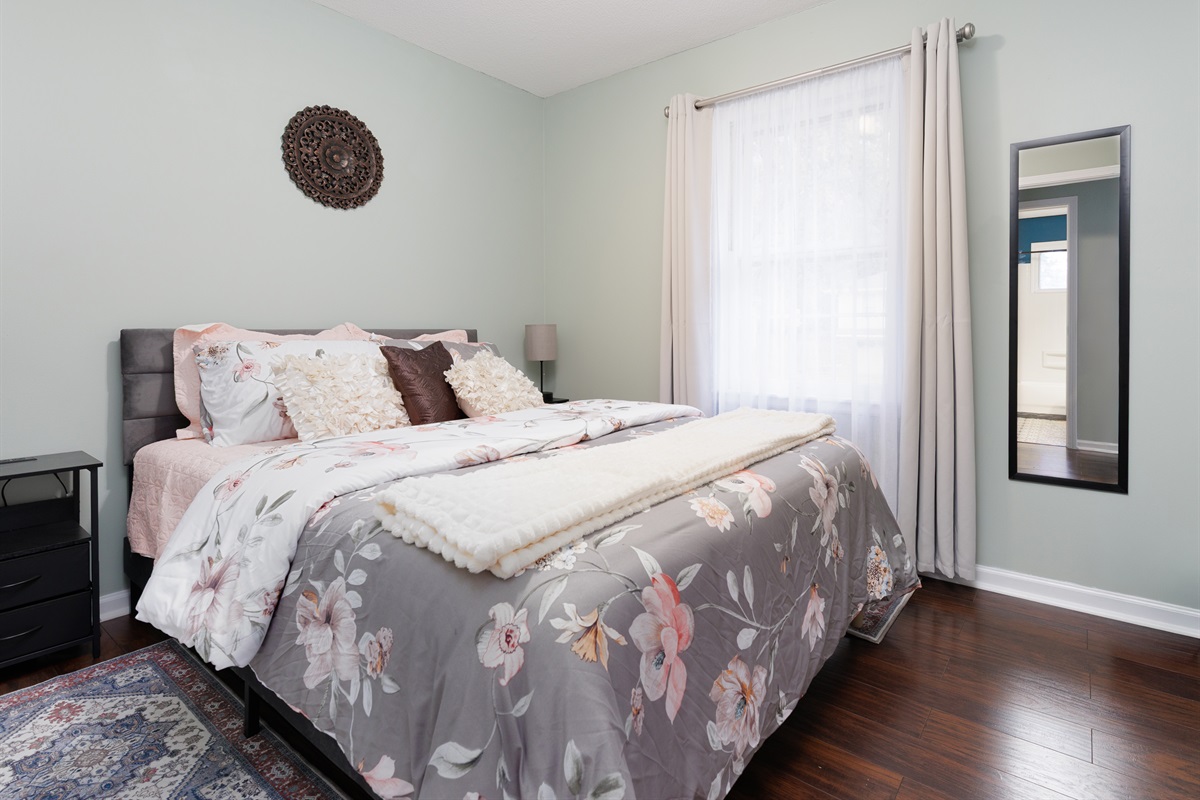 Additional guest bedroom with queen bed, hardwood floors, and a bright, airy feel.