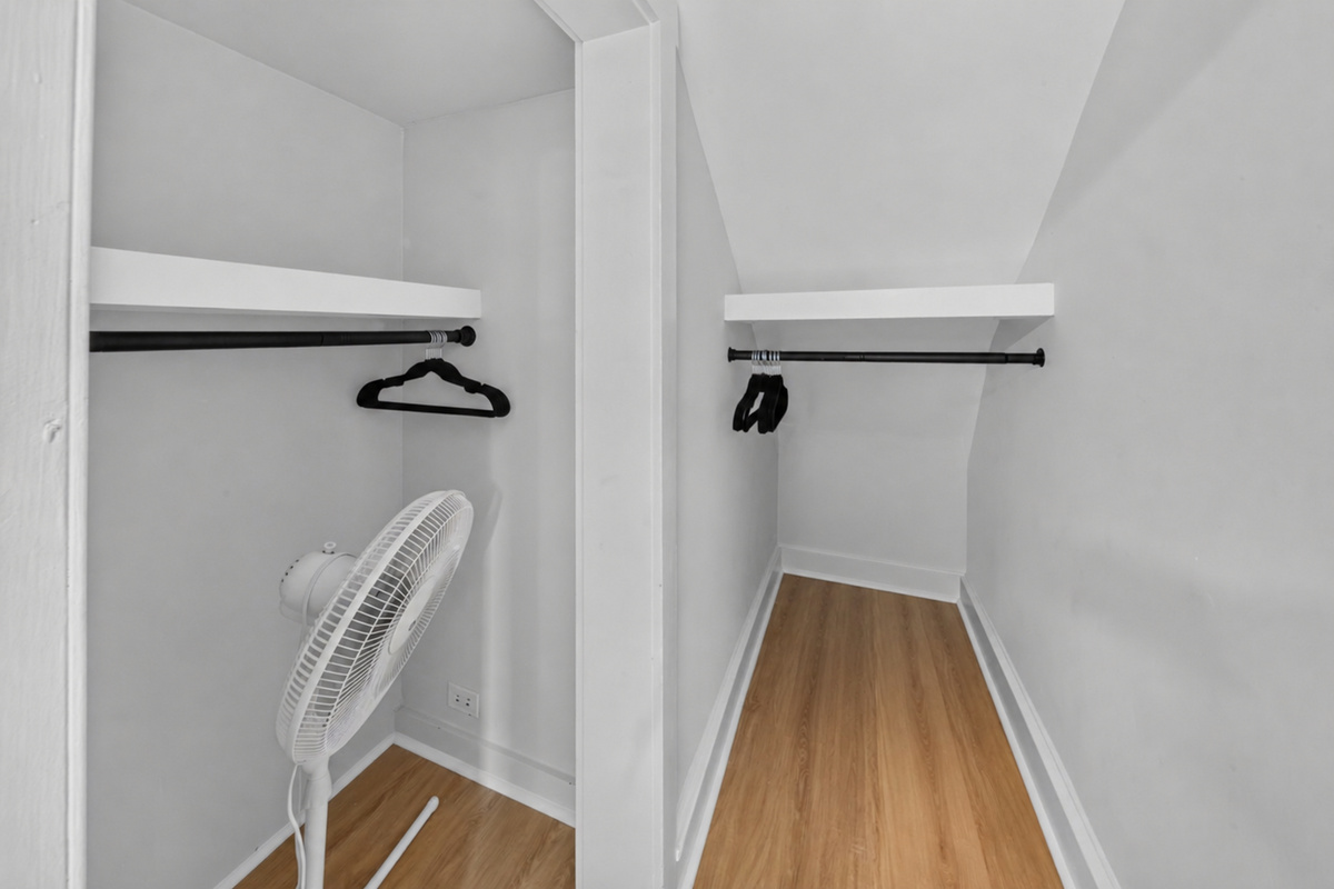 Generous walk-in closet space with hangers, luggage space, and supplemental floor fan.