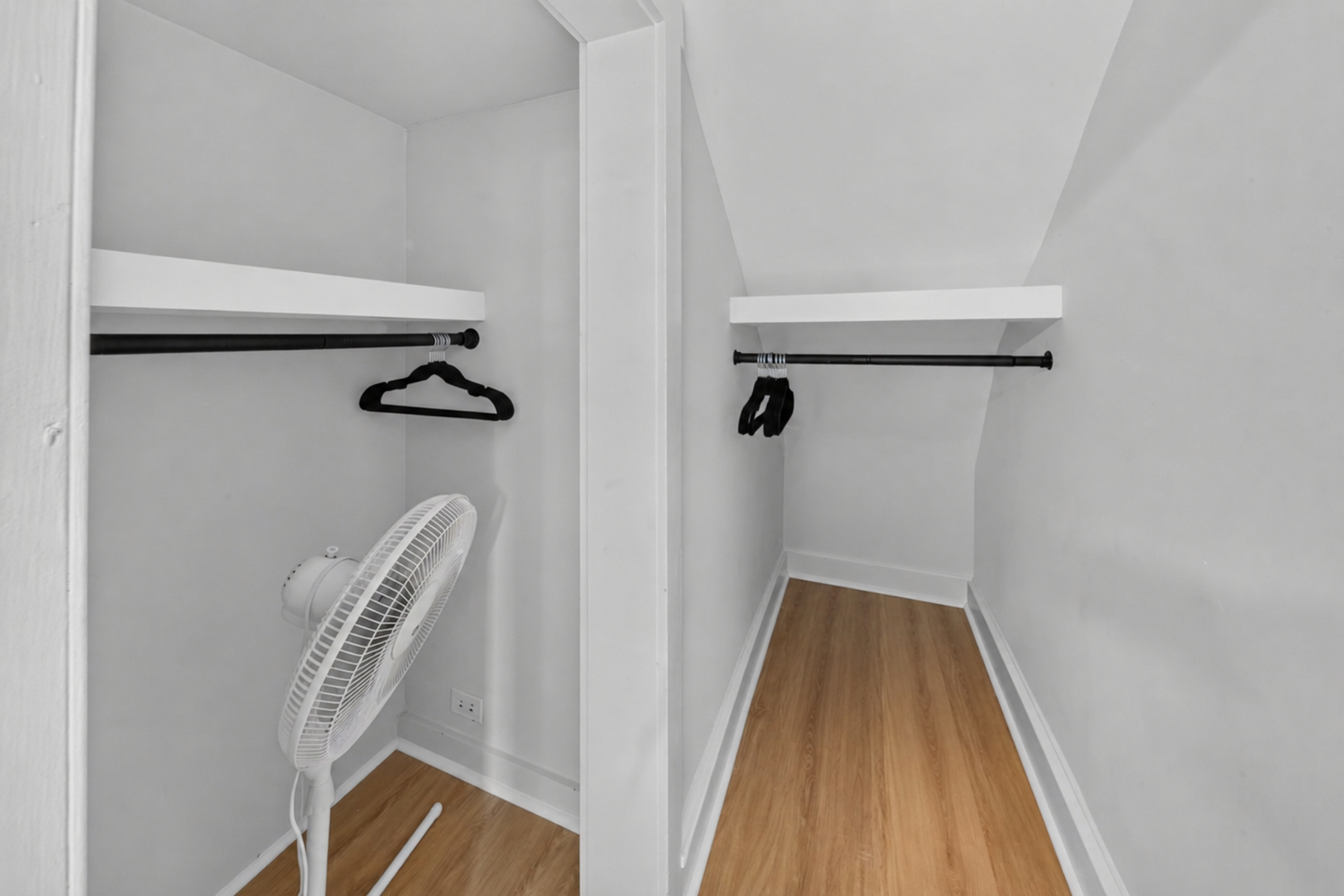 Generous walk-in closet space with hangers, luggage space, and supplemental floor fan.