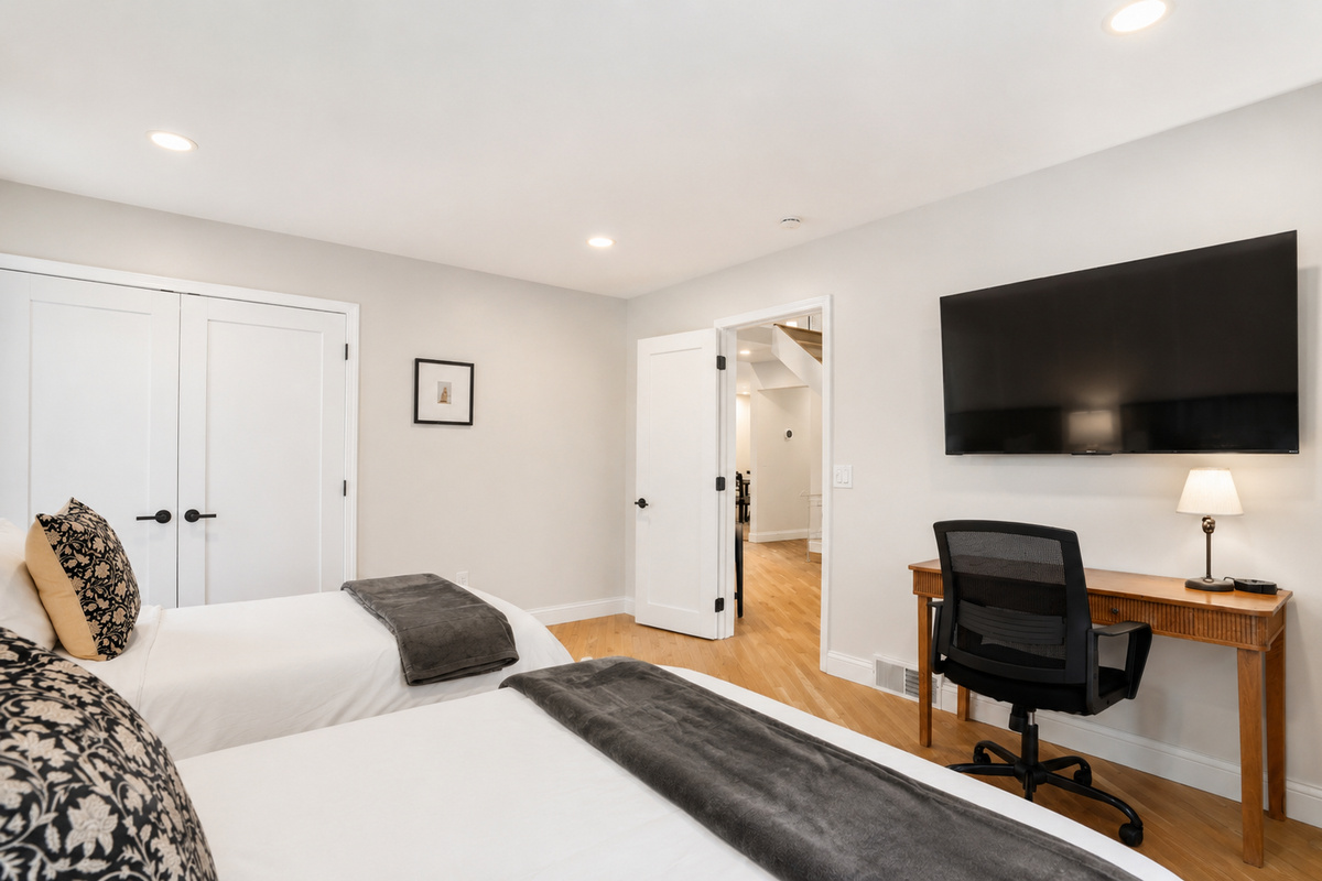 Bright, modern bedroom with cozy bedding, ample natural light, and a work desk—perfect for a relaxing stay.
