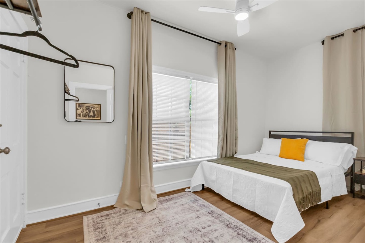 Bedroom with cozy queen bed, plush bedding, exposed closet with hangers, room darkening shades, and fresh decor.