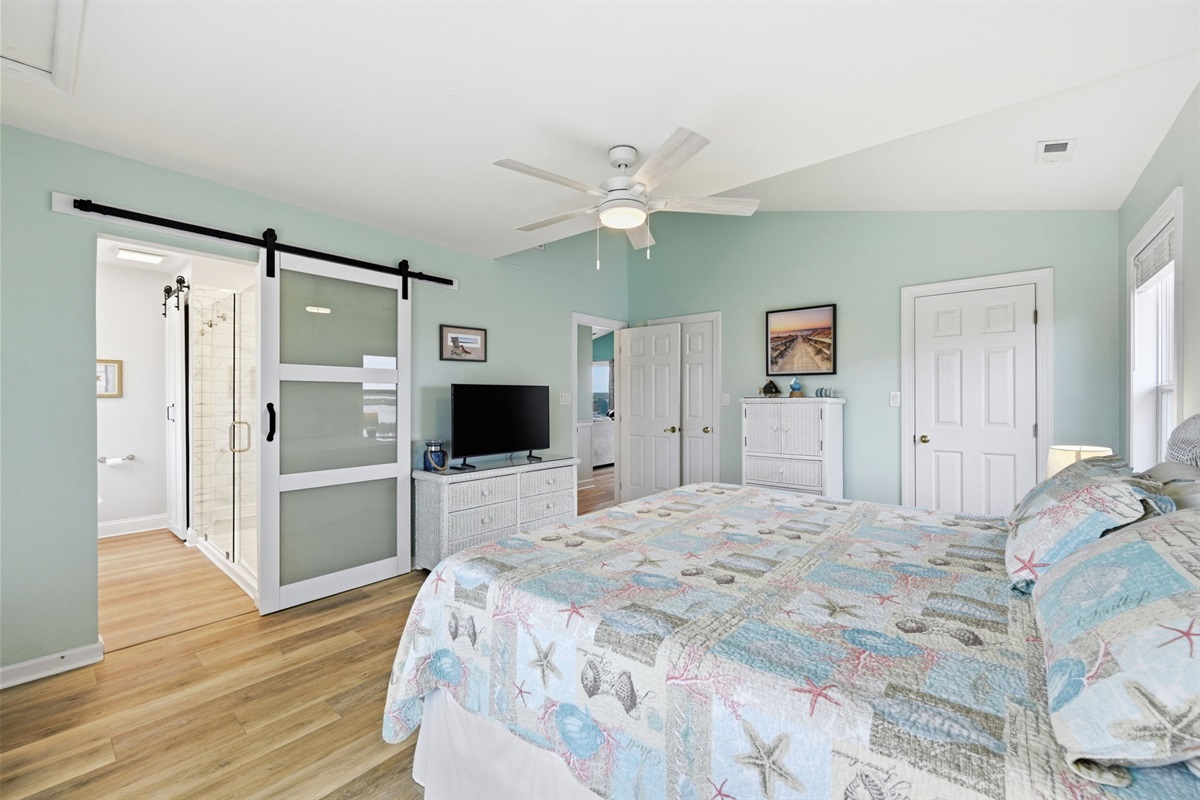 Rest easy in this spacious bedroom featuring a comfortable king sized bed, elevated ceilings, ceiling fan, and a spa-like ensuite bathroom