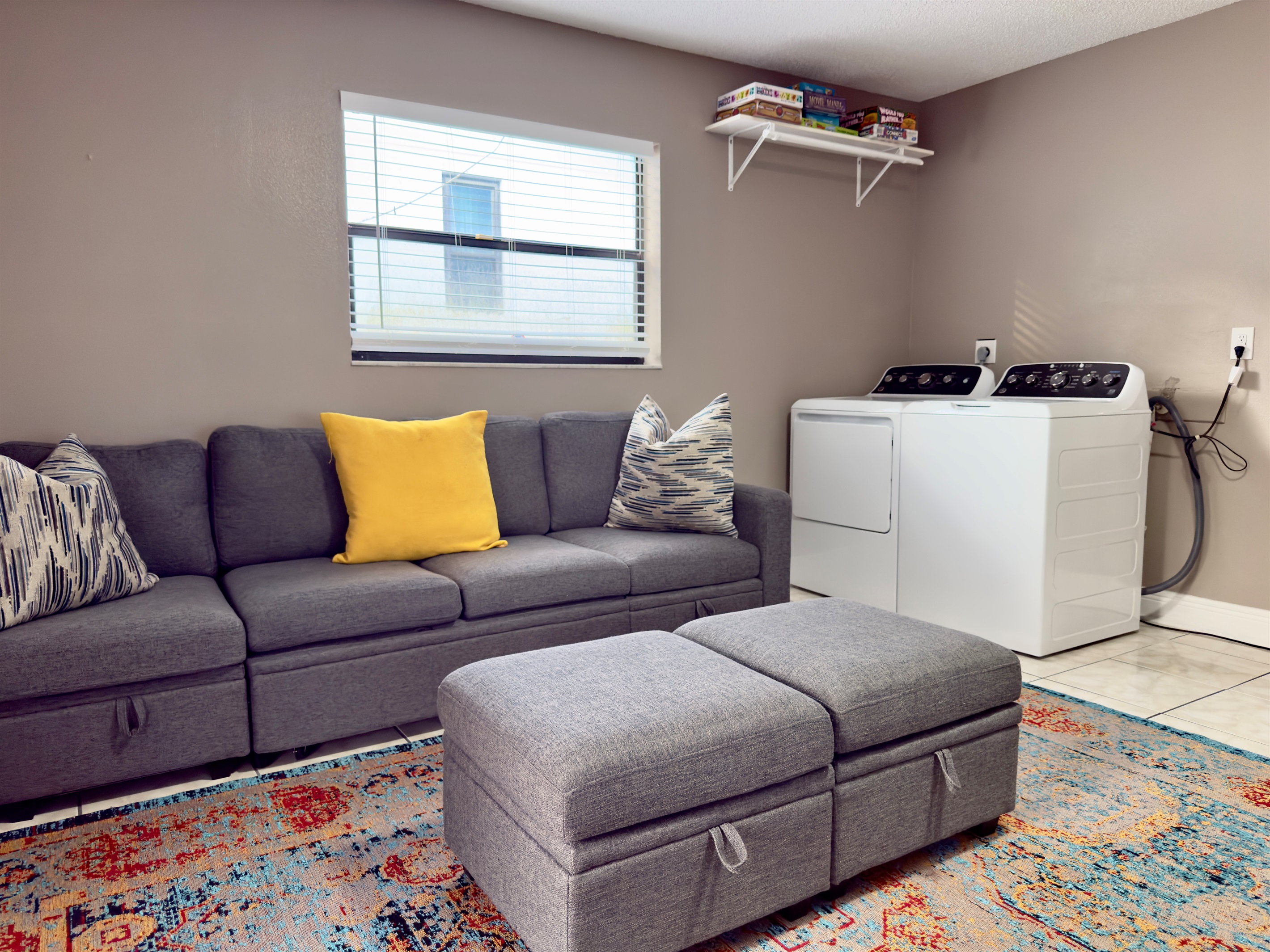 The centerpiece of the room is a modern gray sectional couch, plush and roomy, complete with a pair of matching ottomans for extra legroom or casual seating.