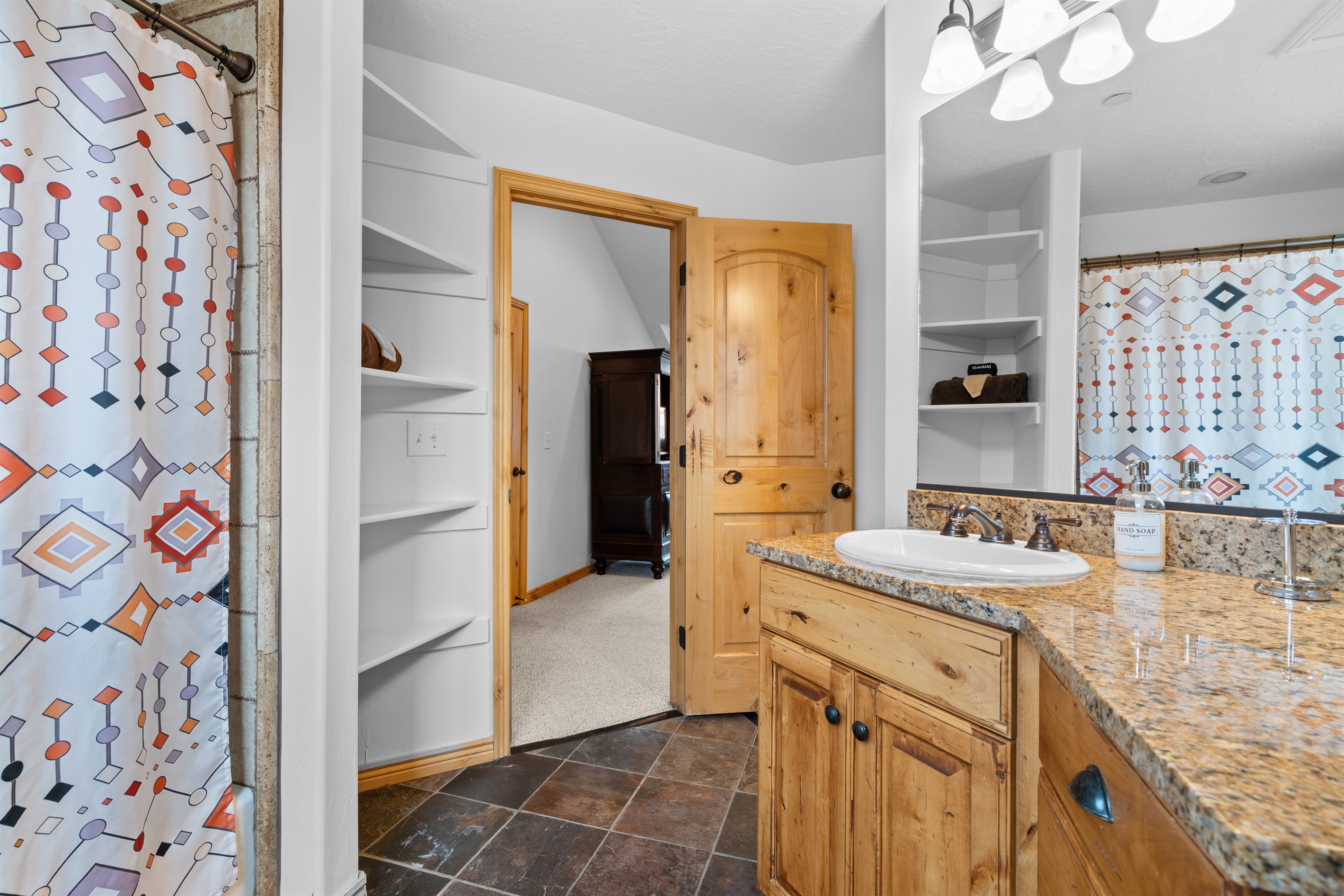 Well-appointed primary bathroom featuring a granite countertop, open shelving, and fresh, modern finishes.