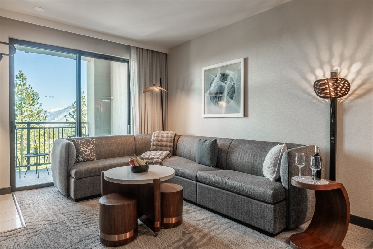 Sierra Point offers a spacious sectional sleeper in the living area, facing the fireplace and creating a cozy place to relax after a day exploring Mammoth. The glass door leading to the private balcony provides warm light.