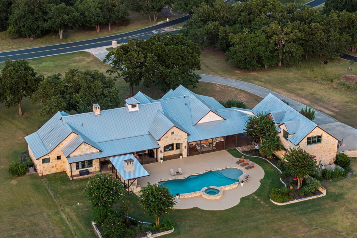 Bird's-eye perspective of a beautiful home and its expansive grounds, featuring a sparkling swimming pool and hot tub.