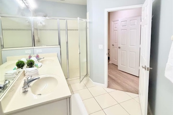 Bright bathroom with a spacious vanity, large mirror, tile flooring, and a walk-in shower with glass doors.