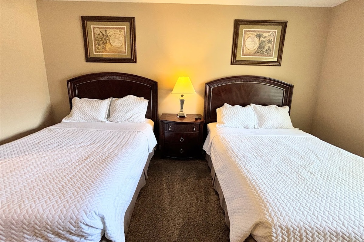 Inviting bedroom with two comfortable beds, matching nightstand, and warm lighting — perfect for guests or family stays.