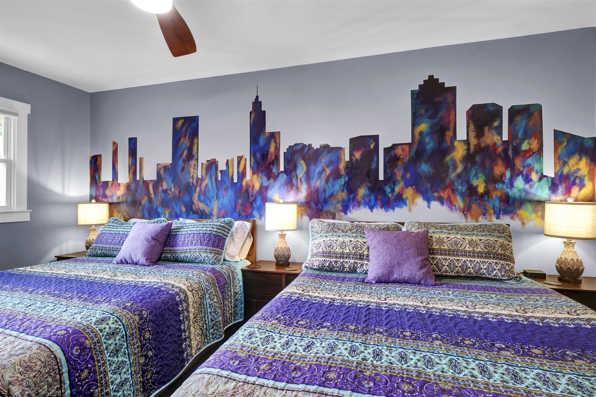 This bedroom features a custom Raleigh skyline mural and two plush queen-sized beds. 