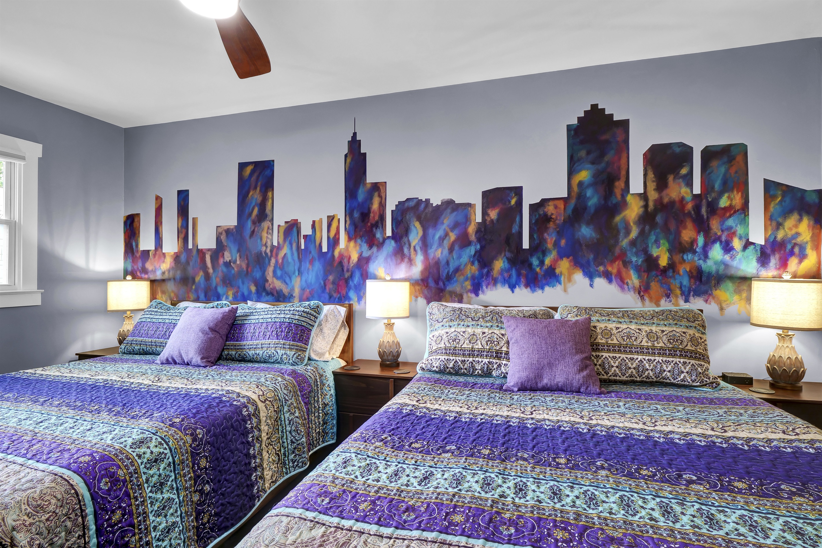 This bedroom features a custom Raleigh skyline mural and two plush queen-sized beds. 