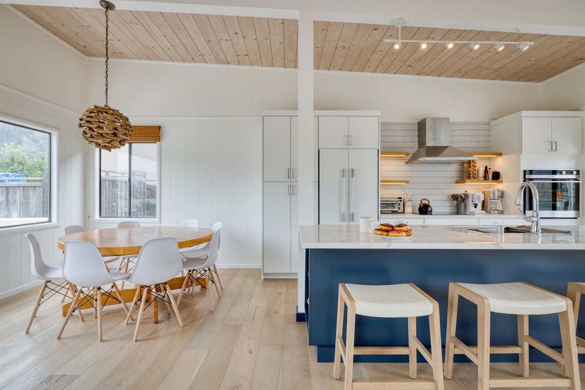 - Dining space with round table and modern chairs for shared meals  
- Kitchen features a navy island with bar seating for casual dining  
- Light wood flooring and ceiling create a warm, coastal inspired vibe  
