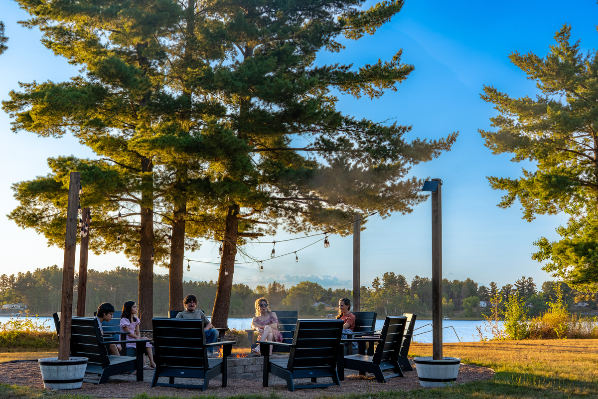 The lakeside fire pit with string lights and Adirondack chairs — where the whole group ends up every single night. Firewood included!