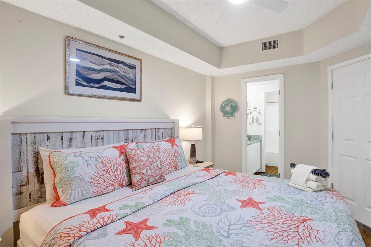 Primary bedroom with king bed, wall mounted smart TV, ceiling fan and en-suite bathroom 