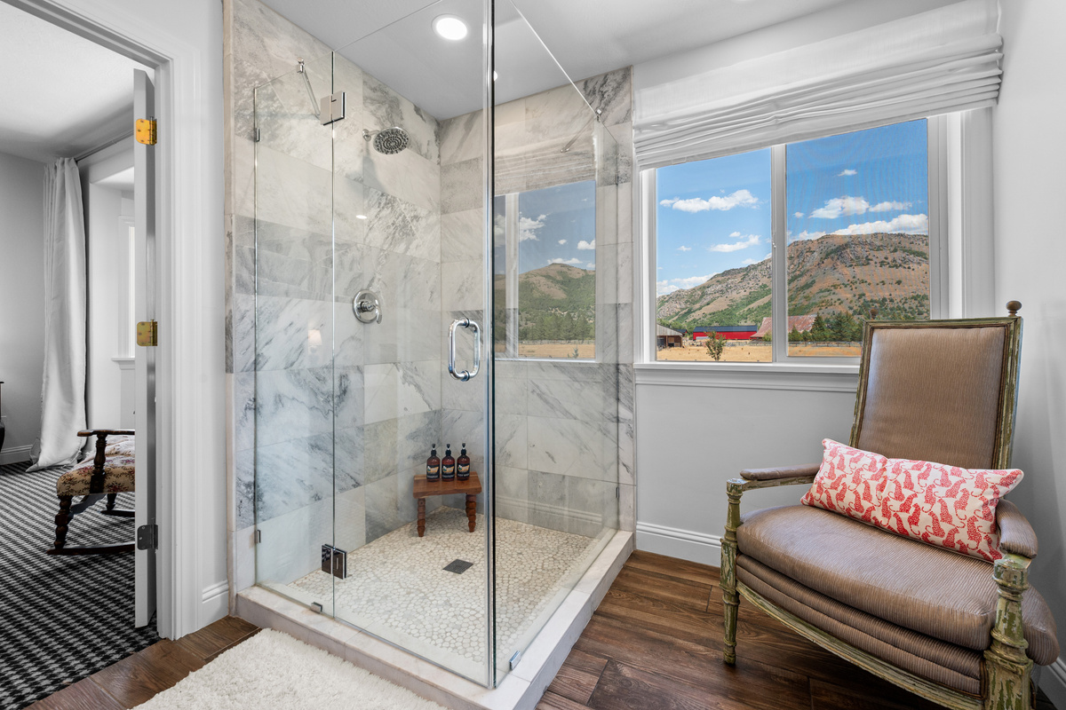 A glass-enclosed marble shower with a rainfall showerhead creates a serene, spa-like setting, complemented by natural light and sweeping mountain views.
