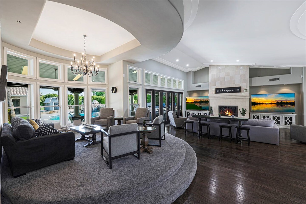 Gather in style in this expansive living space featuring a sophisticated sunken lounge, cozy fireplace, and walls of windows bringing in natural light and poolside views.