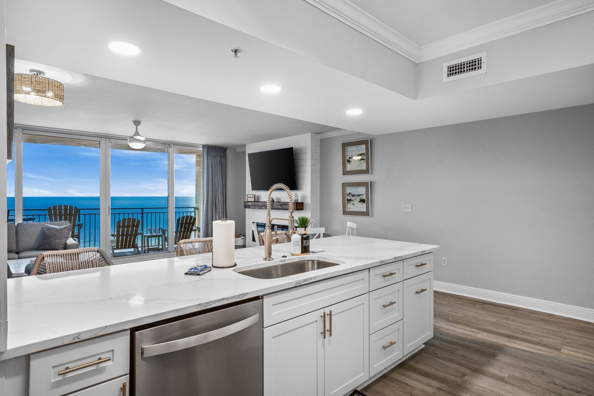 Modern kitchen with quartz countertops and stainless steel appliances, opening to a bright living area and private balcony with breathtaking Gulf views.