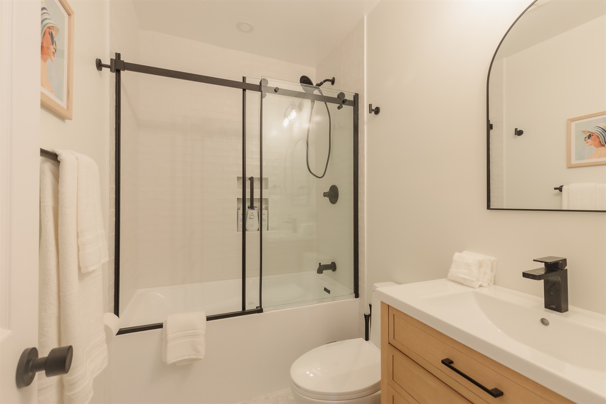 Refresh in style: this modern bath features a sleek glass‑sliding shower/tub, matte‑black fixtures, and hotel‑quality towels to help you unwind after a day exploring San Diego