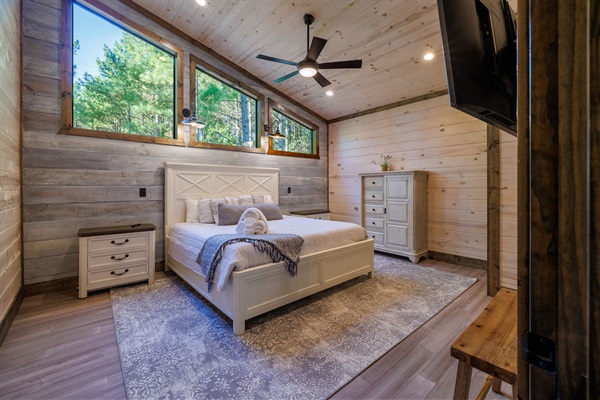 Bright and airy bedroom with high ceilings, a king-size bed, large windows, a cozy sitting area, and modern rustic décor. The ultimate luxury cabin retreat with nature views.