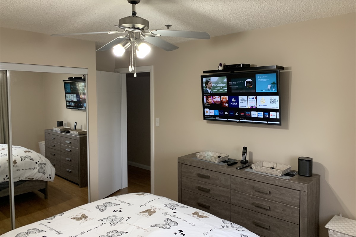 Second bedroom has large mirrored closet, queen bed set, dresser, end table and smart TV and Sonos speaker.