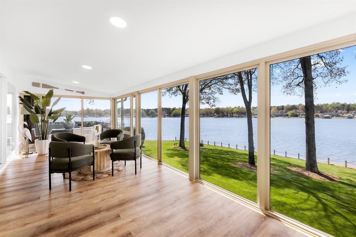 The enclosed sunroom is the star of this home with wall-to-wall windows, panoramic lake views, lounge seating, a couch, and a Smart TV.