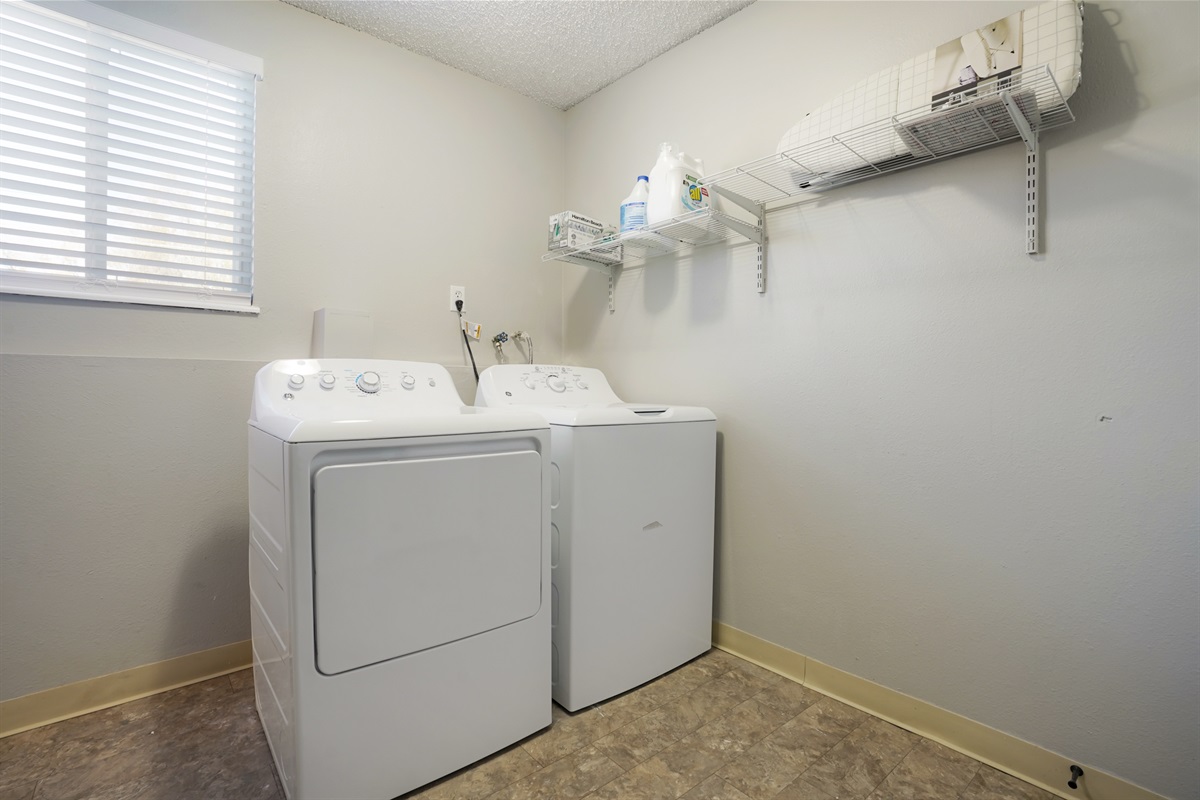 Laundry room equipped with full sized machines, detergent and an iron and ironing board.