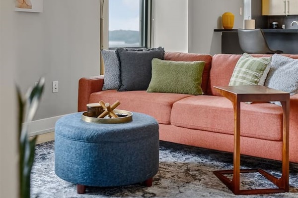 Relax into a vibrant sofa with plush pillows, golden arc lamp, and a chic ottoman centerpiece. This inviting lounge nook is designed for both comfort and style, ideal for evenings in.