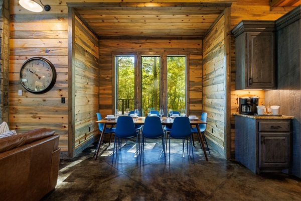A cozy breakfast nook with large windows and forest views offers the perfect spot for morning coffee. Featuring modern rustic design, this dining space adds warmth to a vacation rental, making every meal a relaxing nature retreat moment.