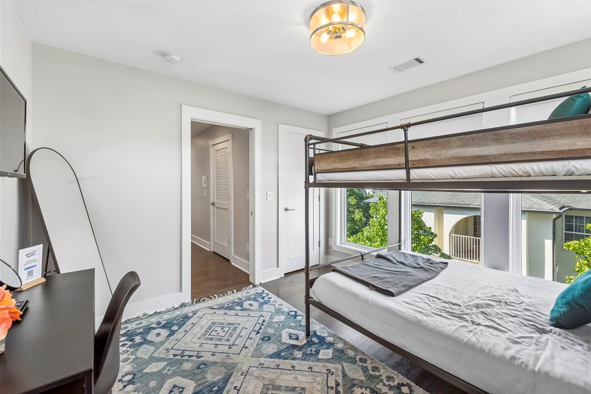 Queen over Queen bunk framed by oversized windows & natural light - Soft layered bedding with patterned pillows create a cozy and inviting sleep space - Easy access to hallway & shared areas makes this room perfect for families or groups