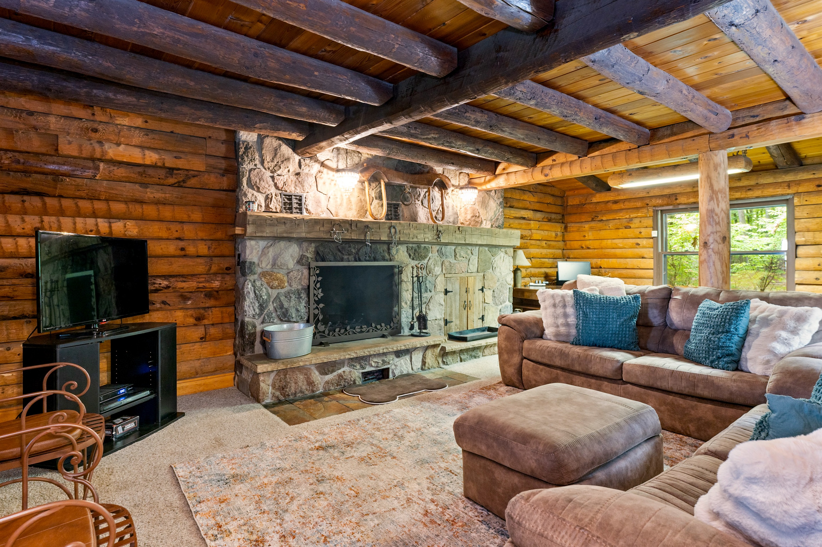 Charming log cabin living room featuring exposed beams, a grand stone fireplace, and plush seating for ultimate relaxation.
