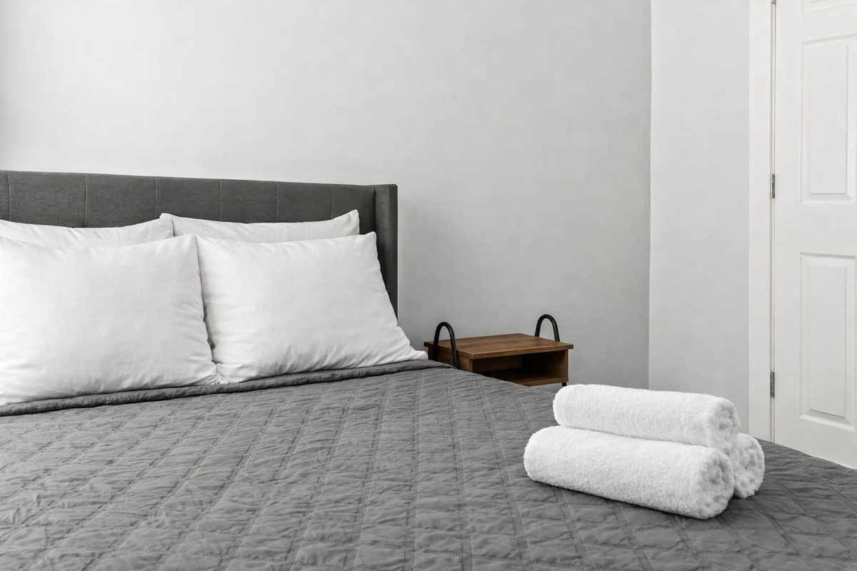 Clean and inviting sleeping area with full-size bed, folded towels, and convenient bedside storage.