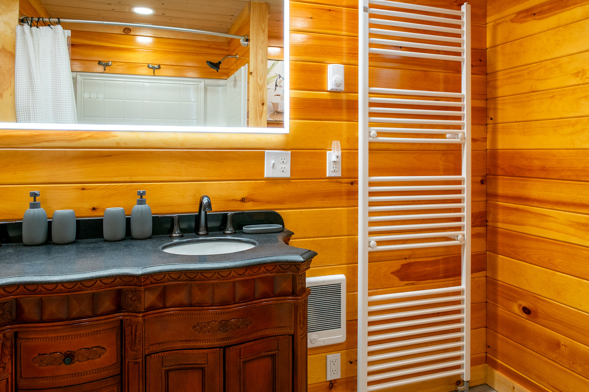 Prepare for the day ahead at the elegant carved-wood vanity station. This tighter view highlights the stone counter, matching matte gray accessories, the dedicated wall heating vent, and the reflection of the shower area in the LED mirror.