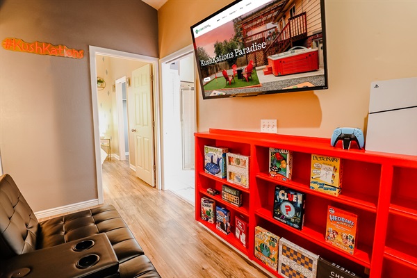 A vibrant setup featuring a TV atop a red cabinet, alongside a PS5 and a collection of board games, creating a colorful and engaging entertainment hub.