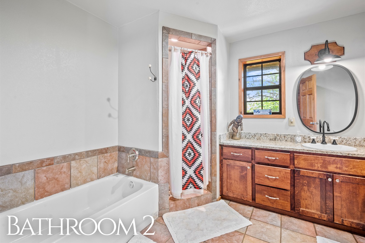Bright and spacious with a soaking tub, granite counter, and large mirror.
