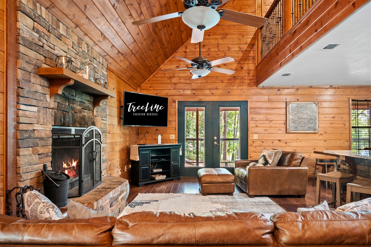 Relax fireside in the vaulted living room featuring a Smart TV, plush leather seating, and forest views.